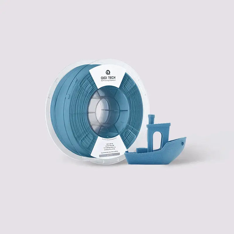 Spool of blue 3D printer filament with a matching Benchy calibration boat model on a light background.