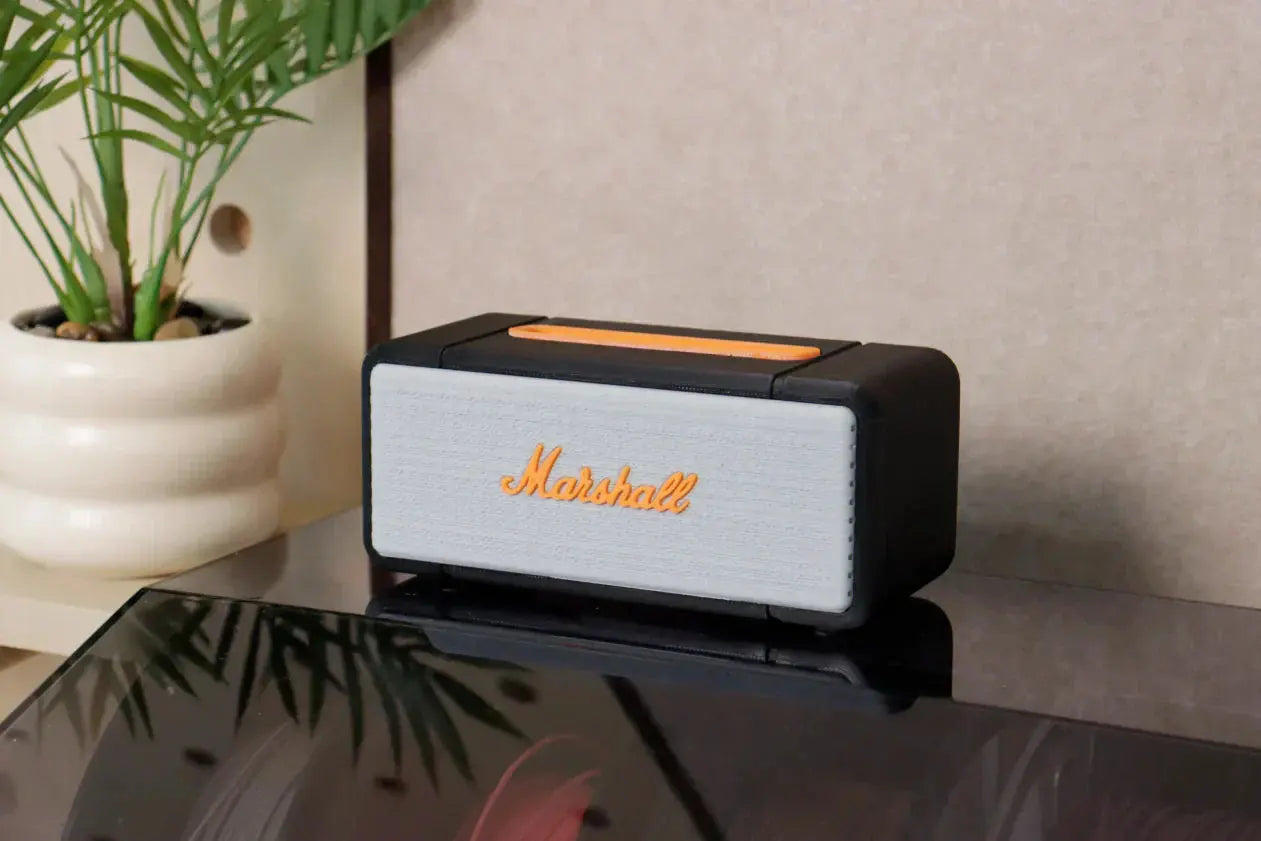 A 3D-printed miniature speaker model, with a gray mesh and orange logo, is placed next to a plant pot on the table.