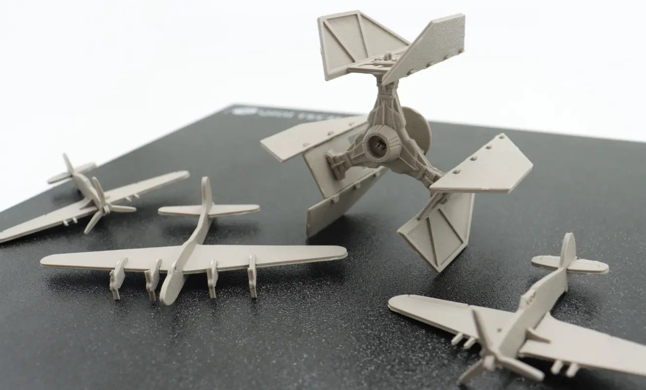 A collection of 3D printed airplane and aircraft - like models placed on a printing surface.